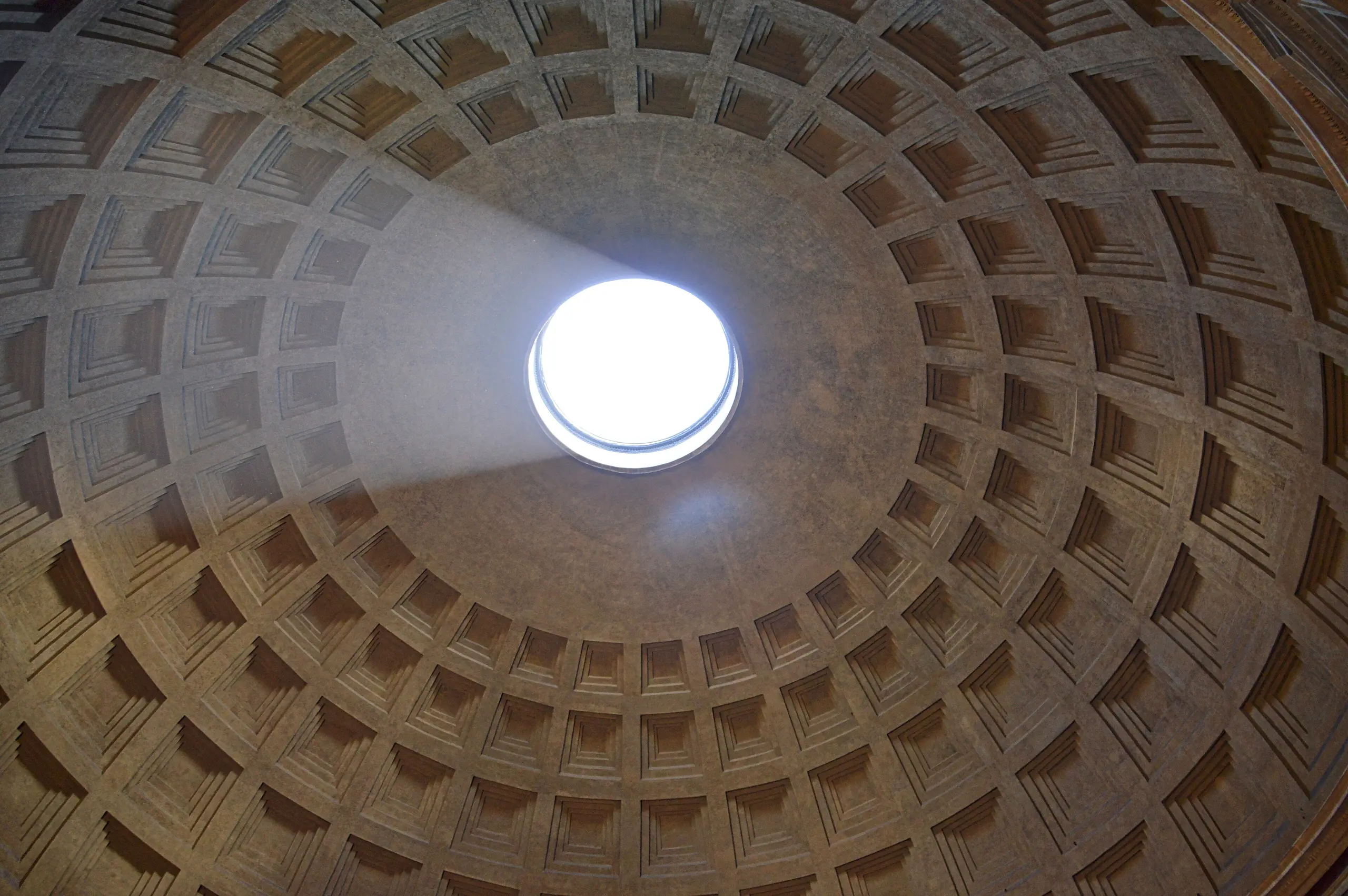 Looking up into the Pantheon's coffered dome as a shaft of sunlight pours through the oculus and rakes across the stone.