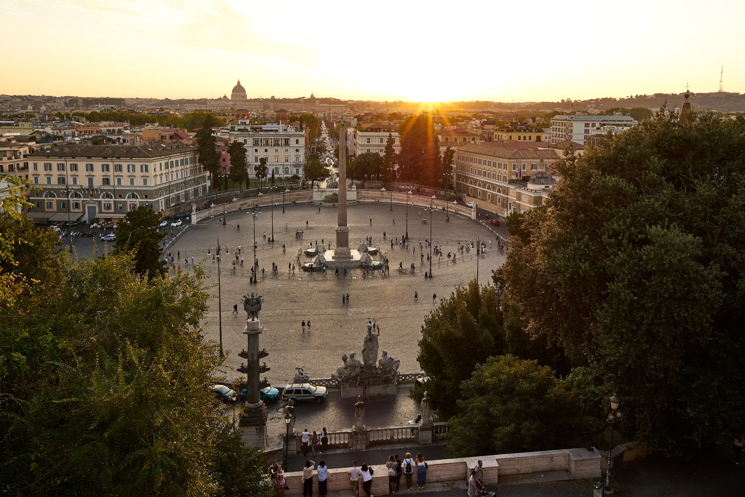 The sun low over Piazza del Popolo and the distant dome of St Peter's, seen from the Pincio terrace at golden hour.