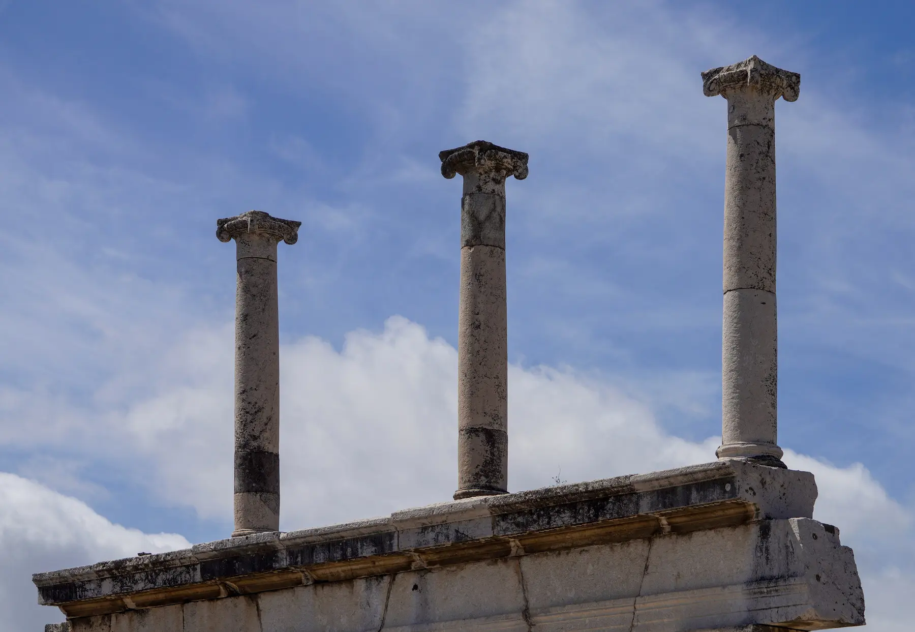 Three standing columns of Pompeii's forum against a blue sky with scattered clouds.
