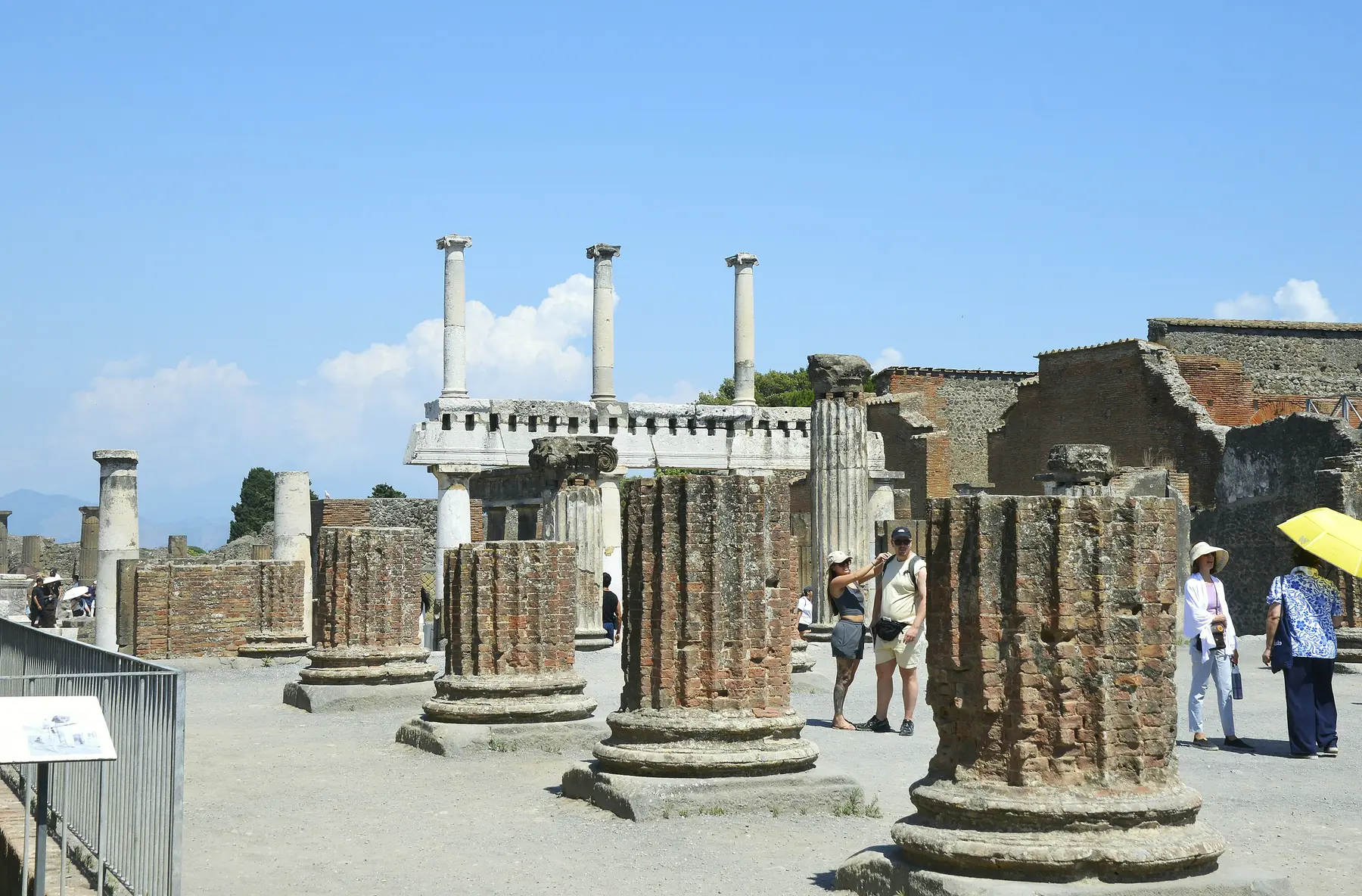 Fluted column drums and a white-capped colonnade in the Forum of Pompeii under a blue sky.